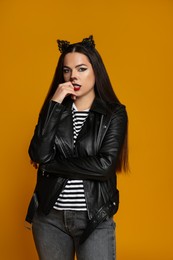 Photo of Woman with cat makeup and ears in leather jacket on orange background