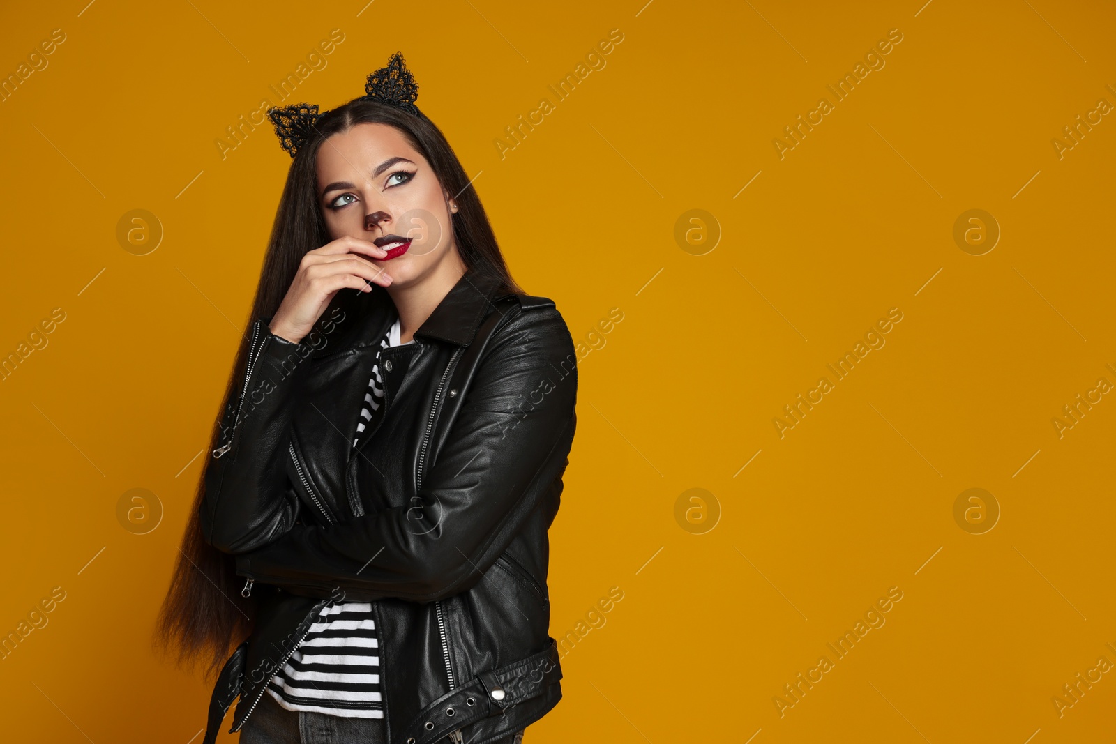 Photo of Woman with cat makeup and ears in leather jacket on orange background. Space for text