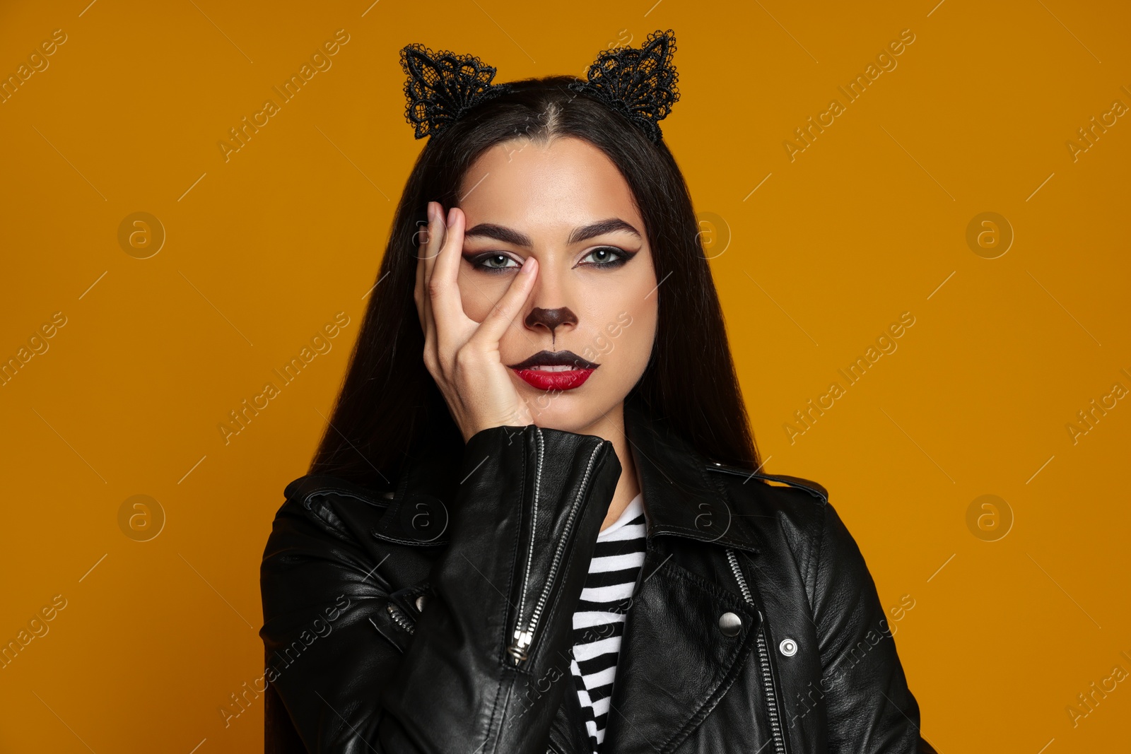 Photo of Woman with cat makeup and ears in leather jacket on orange background