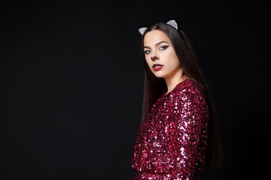 Photo of Charming woman with cat makeup and ears on black background. Space for text