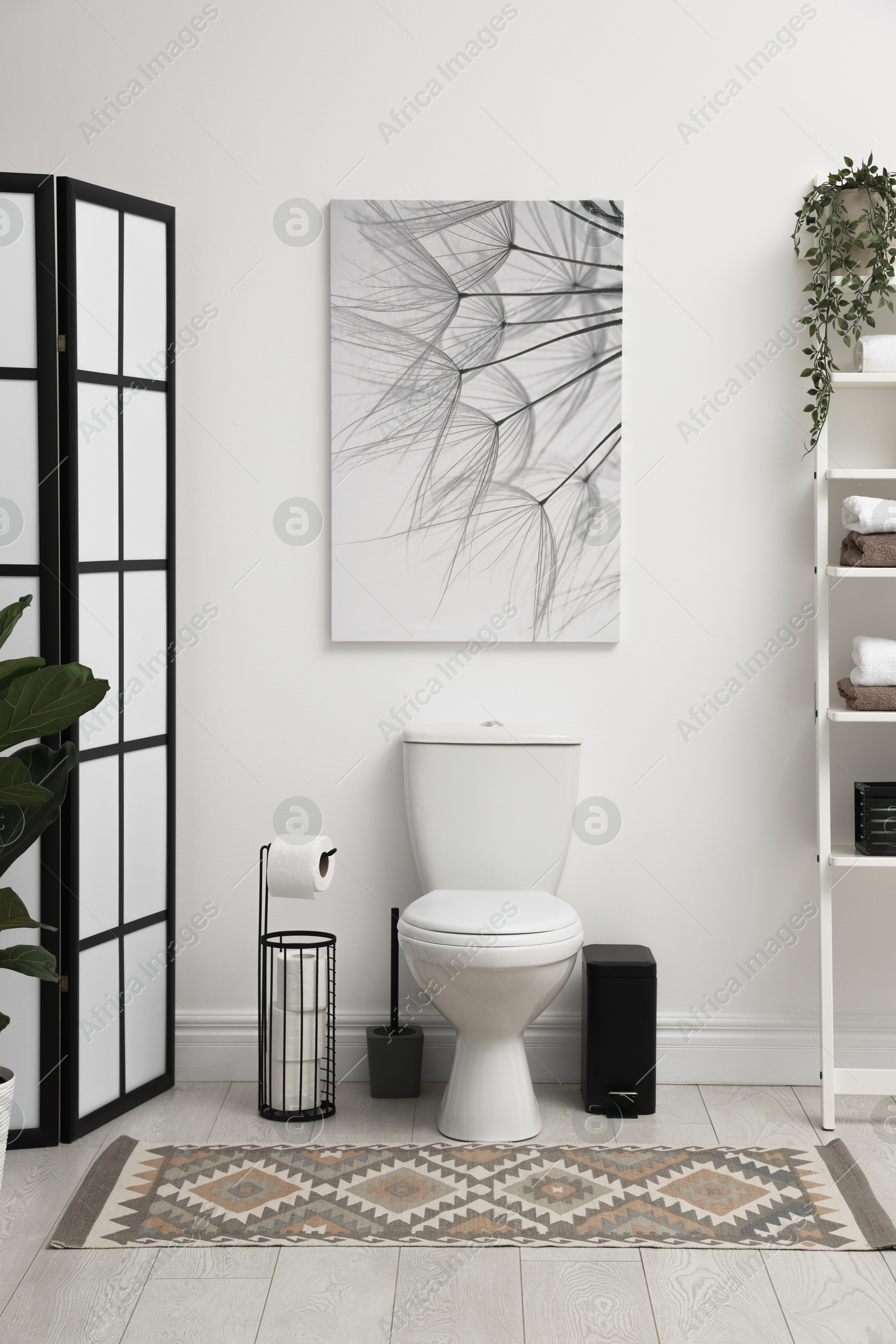 Photo of Stylish restroom interior with folding screen, toilet bowl and houseplant