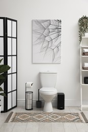 Photo of Stylish restroom interior with folding screen, toilet bowl and houseplant