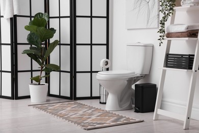 Photo of Stylish restroom interior with folding screen, toilet bowl and houseplant