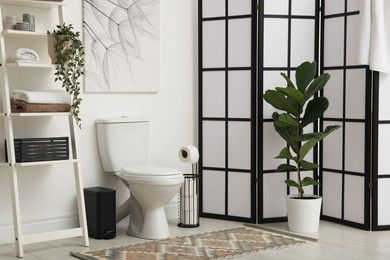 Photo of Stylish restroom interior with folding screen, toilet bowl and houseplant