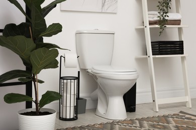 Photo of Ceramic toilet bowl, necessities and houseplants in restroom