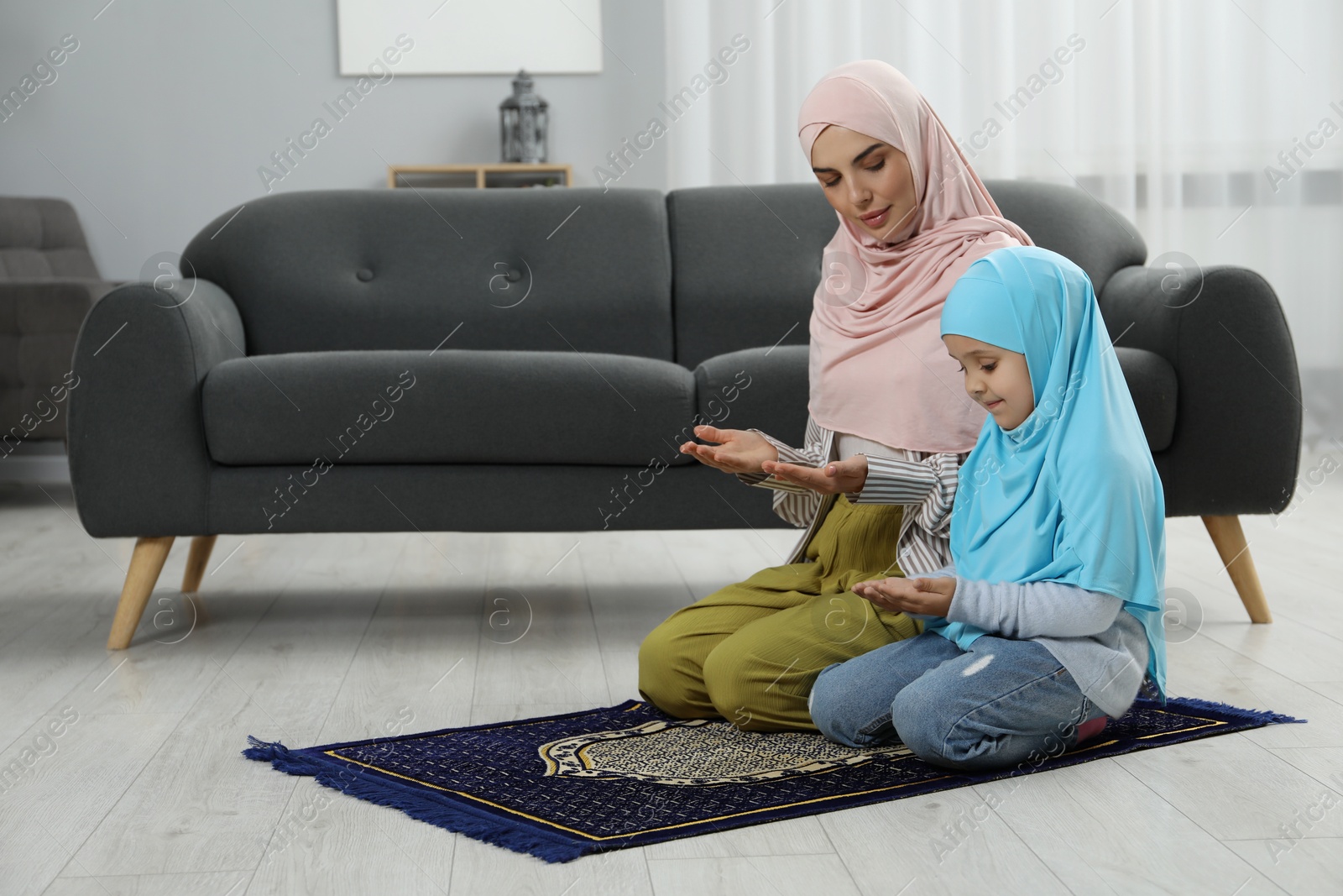 Photo of Muslim woman and her daughter praying on mat at home