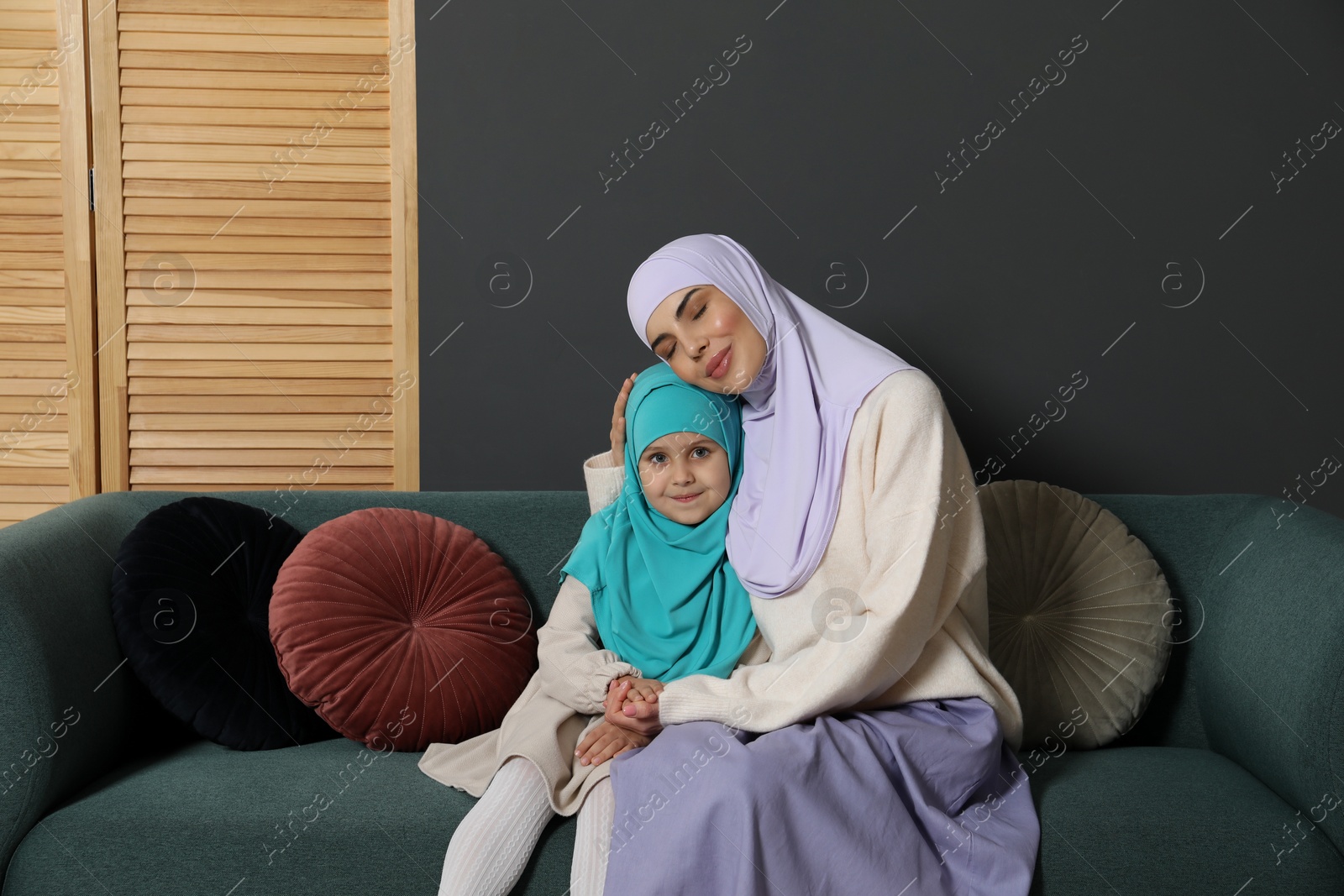 Photo of Muslim woman and her daughter sitting on sofa at home