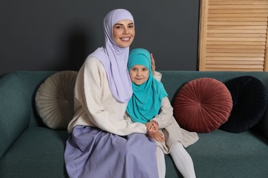 Photo of Muslim woman and her daughter sitting on sofa at home