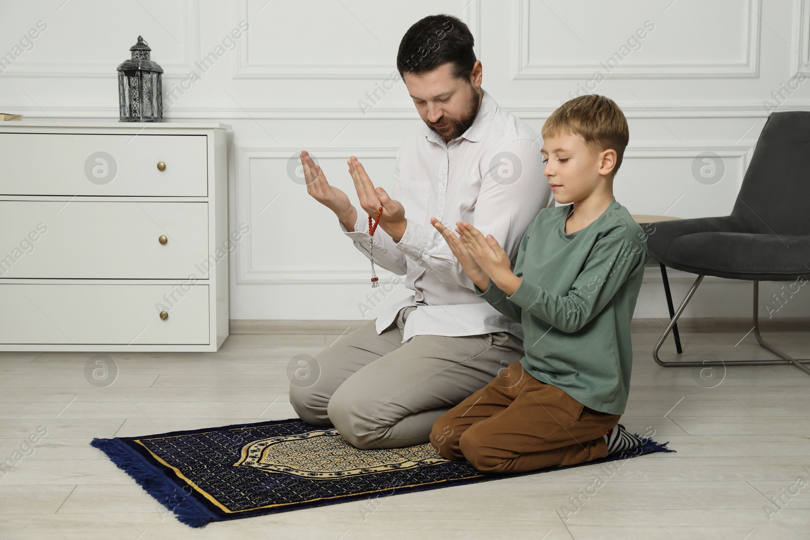 Photo of Muslim man and his son with beads praying on mat at home