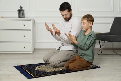 Photo of Muslim man and his son with beads praying on mat at home