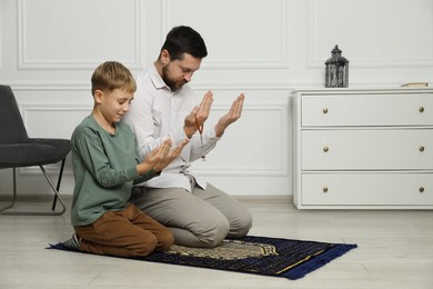 Photo of Muslim man and his son with beads praying on mat at home