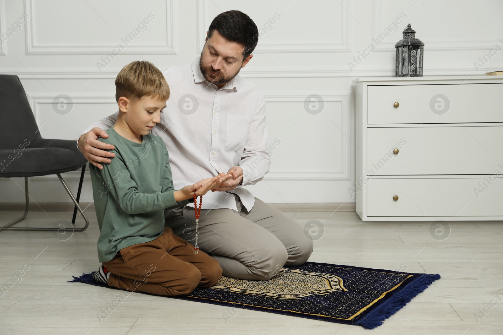 Photo of Muslim man and his son with beads praying on mat at home