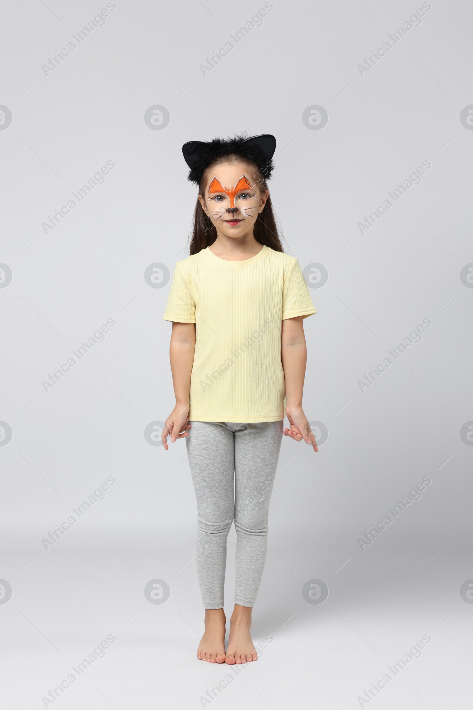 Photo of Cute girl with painted face and ears as cat on grey background