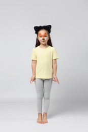 Photo of Cute girl with painted face and ears as cat on grey background