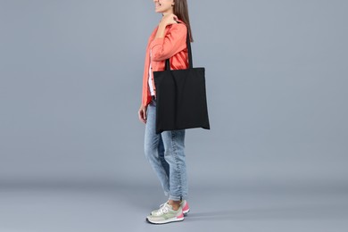 Photo of Woman with blank black shopper bag on grey background, closeup. Mockup for design