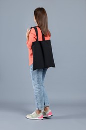 Photo of Woman with blank black shopper bag on grey background, back view. Mockup for design