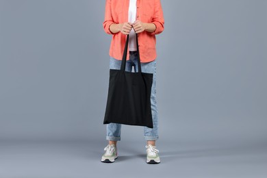 Photo of Woman with blank black shopper bag on grey background, closeup. Mockup for design