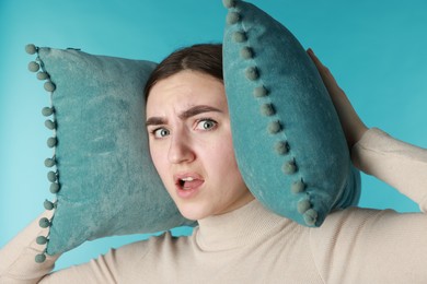 Photo of Distressed woman covering her ears with pillows from loud noise on blue background