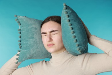 Photo of Distressed woman covering her ears with pillows from loud noise on blue background