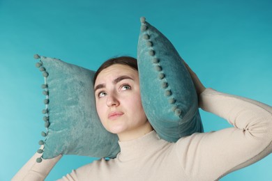 Distressed woman covering her ears with pillows from loud noise on blue background