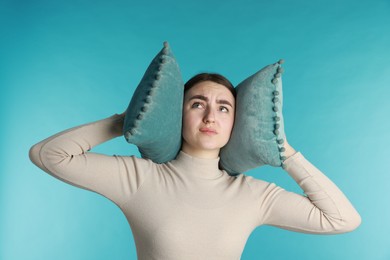 Photo of Distressed woman covering her ears with pillows from loud noise on blue background