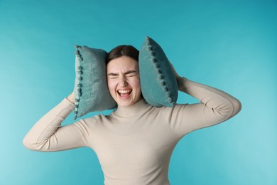 Photo of Frustrated woman covering her ears with pillows from loud noise on blue background