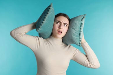 Photo of Frustrated woman covering her ears with pillows from loud noise on blue background