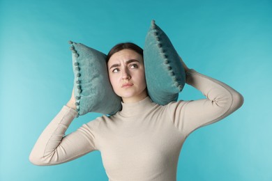 Photo of Frustrated woman covering her ears with pillows from loud noise on blue background