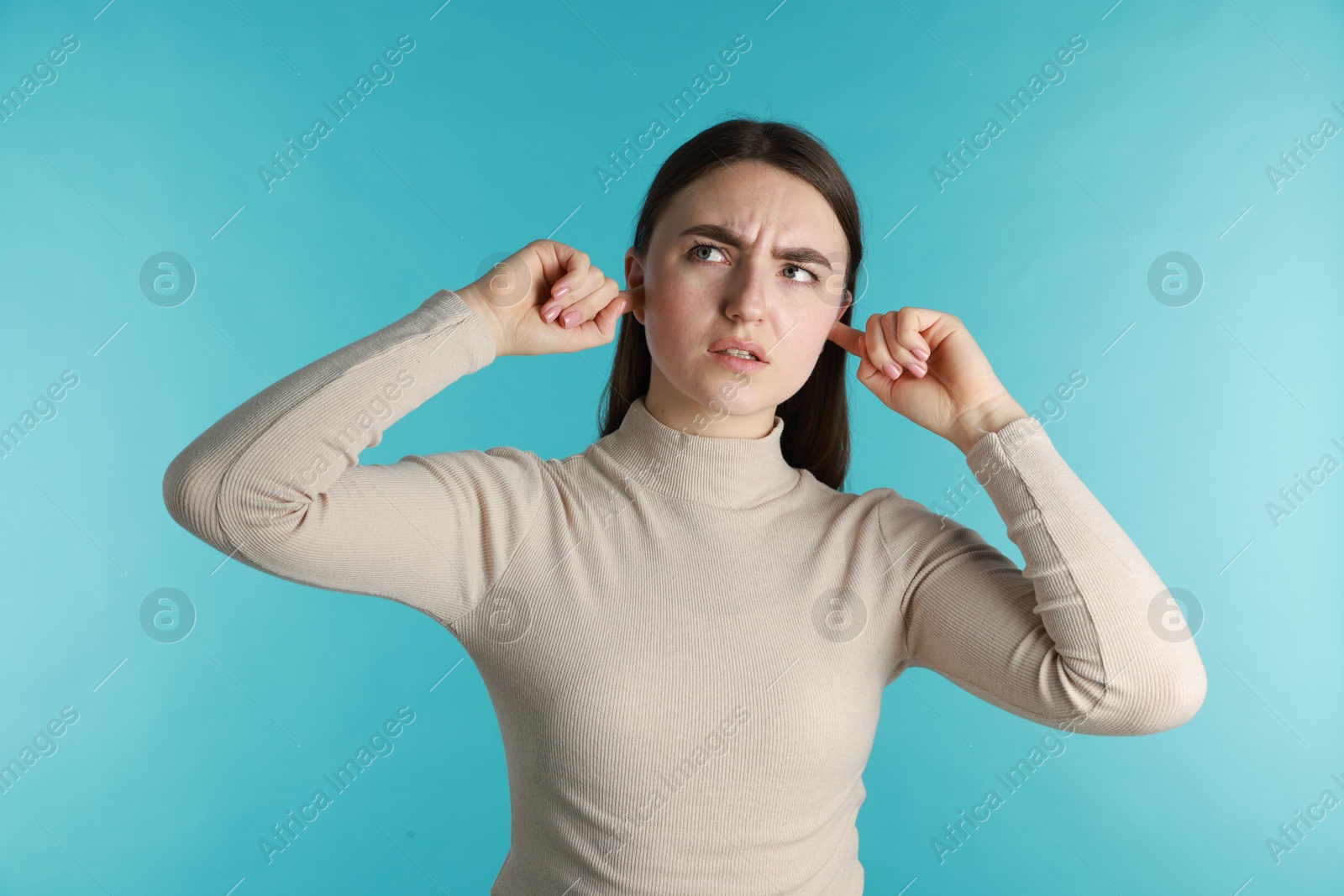 Photo of Frustrated woman covering her ears from loud noise on blue background