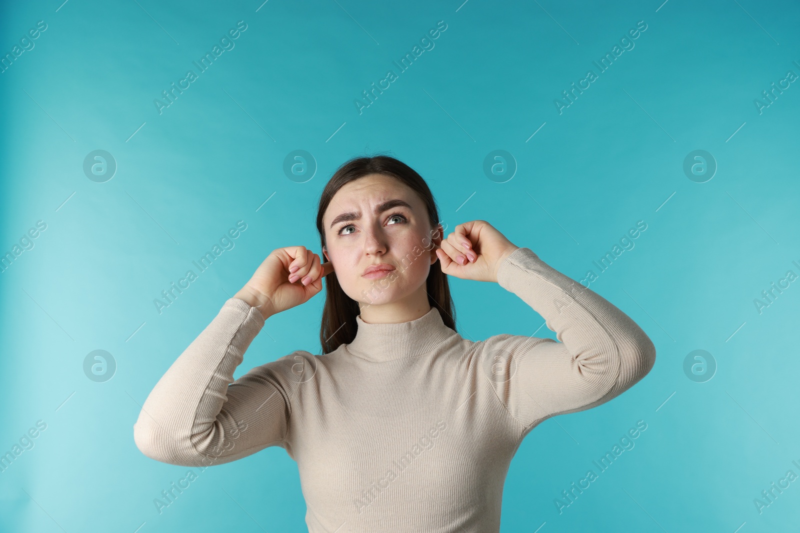 Photo of Frustrated woman covering her ears from loud noise on blue background