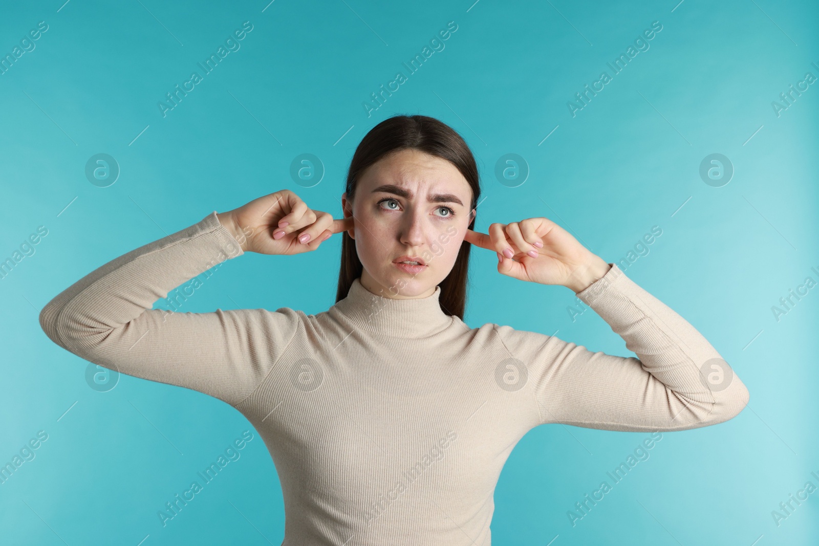 Photo of Distressed woman covering her ears from loud noise on blue background