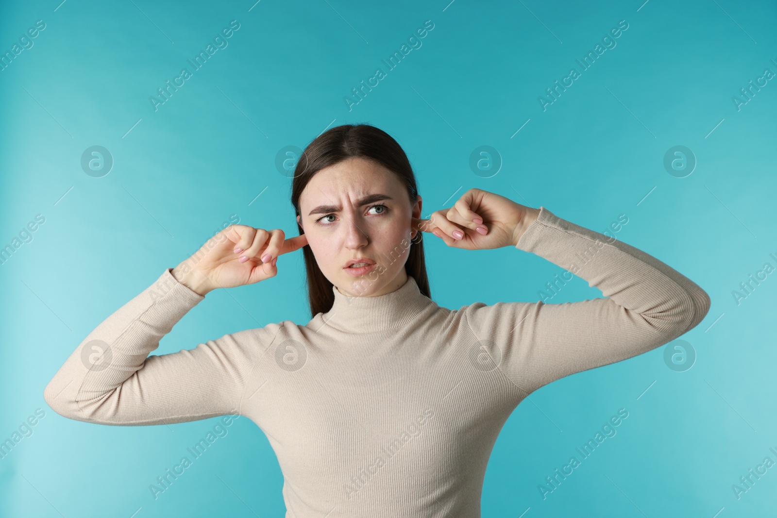 Photo of Frustrated woman covering her ears from loud noise on blue background