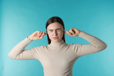 Photo of Frustrated woman covering her ears from loud noise on blue background