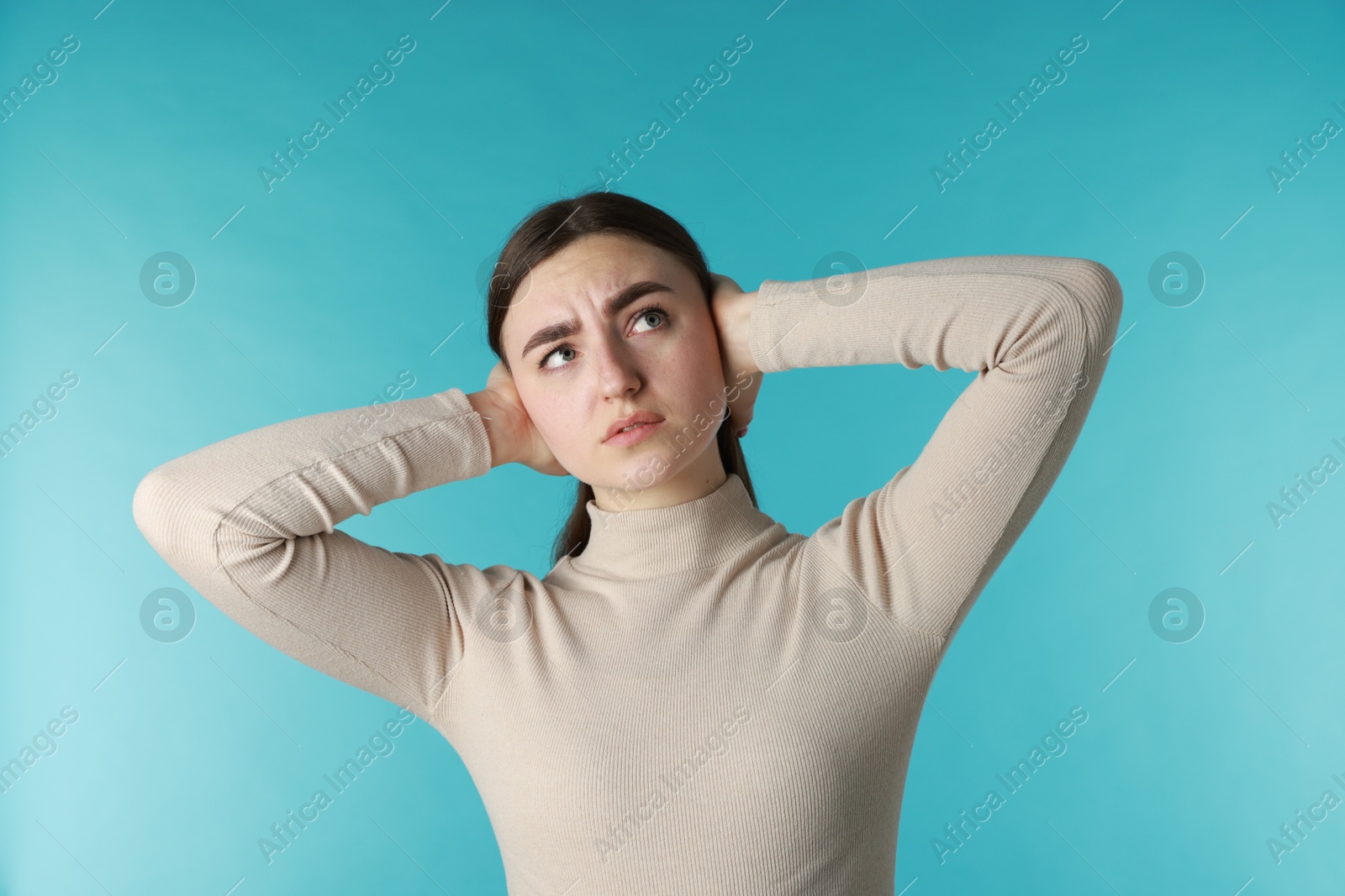 Photo of Distressed woman covering her ears from loud noise on blue background