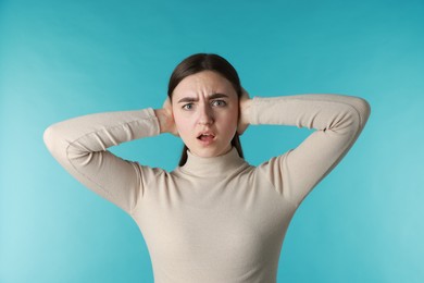 Photo of Distressed woman covering her ears from loud noise on blue background