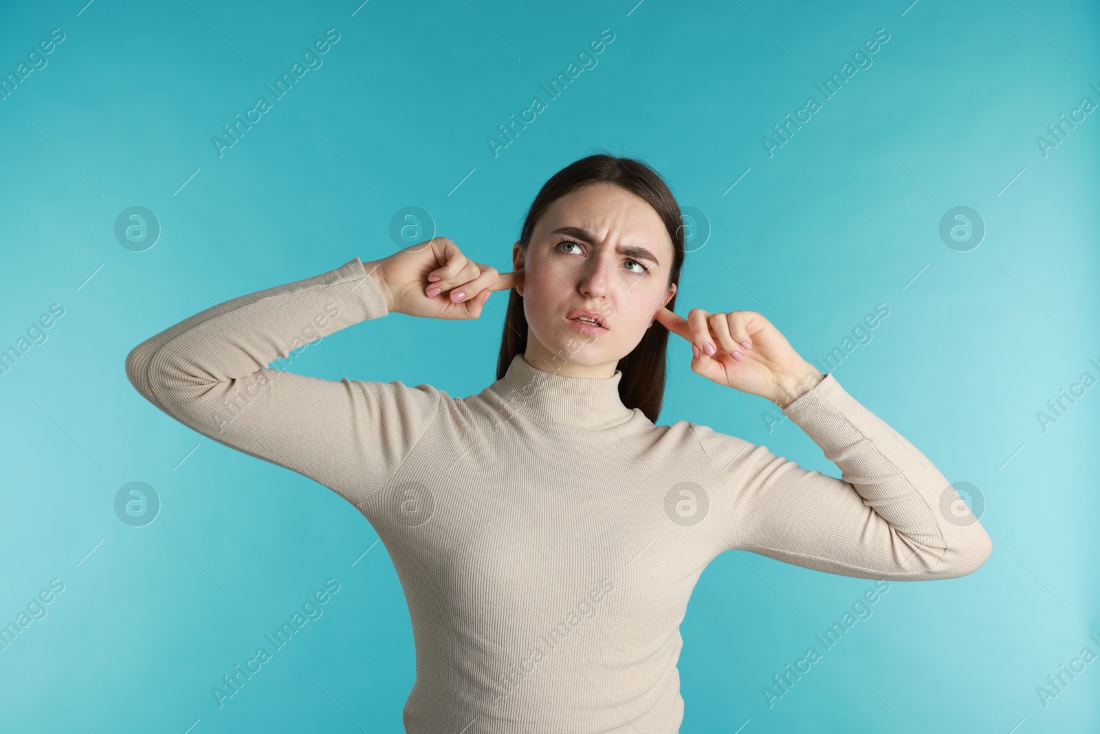 Photo of Frustrated woman covering her ears from loud noise on blue background