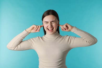 Photo of Frustrated woman covering her ears from loud noise on blue background