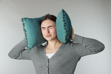 Photo of Distressed woman covering her ears with pillows from loud noise on light grey background