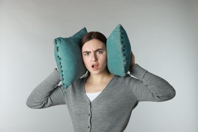 Photo of Distressed woman covering her ears with pillows from loud noise on light grey background