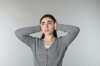 Photo of Distressed woman covering her ears from loud noise on light grey background