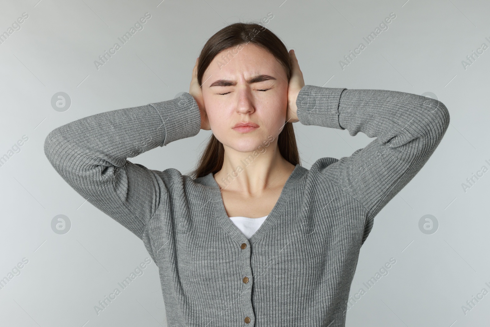 Photo of Distressed woman covering her ears from loud noise on light grey background