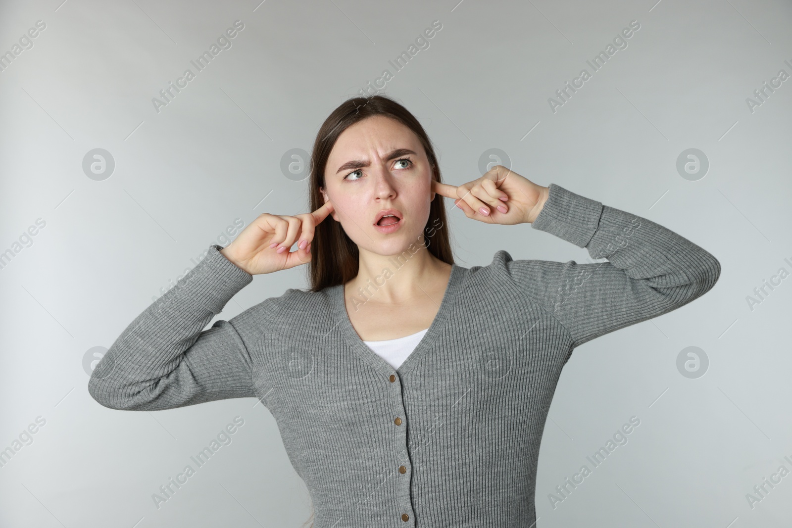 Photo of Distressed woman covering her ears from loud noise on light grey background