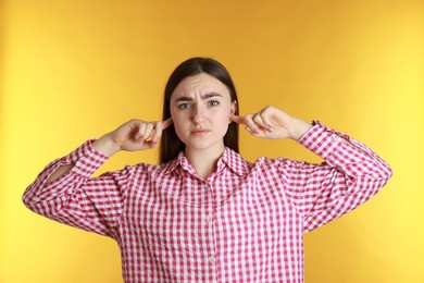 Photo of Distressed woman covering her ears from loud noise on yellow background