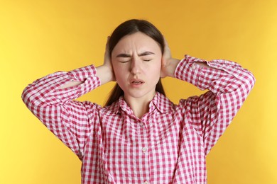 Photo of Distressed woman covering her ears from loud noise on yellow background