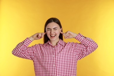 Photo of Distressed woman covering her ears from loud noise on yellow background