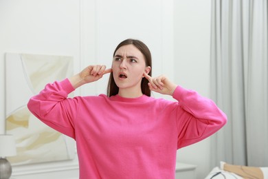 Photo of Annoyed woman covering her ears from loud noise at home