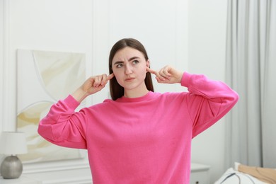 Photo of Annoyed woman covering her ears from loud noise at home