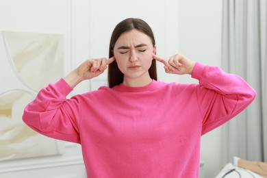 Photo of Annoyed woman covering her ears from loud noise at home