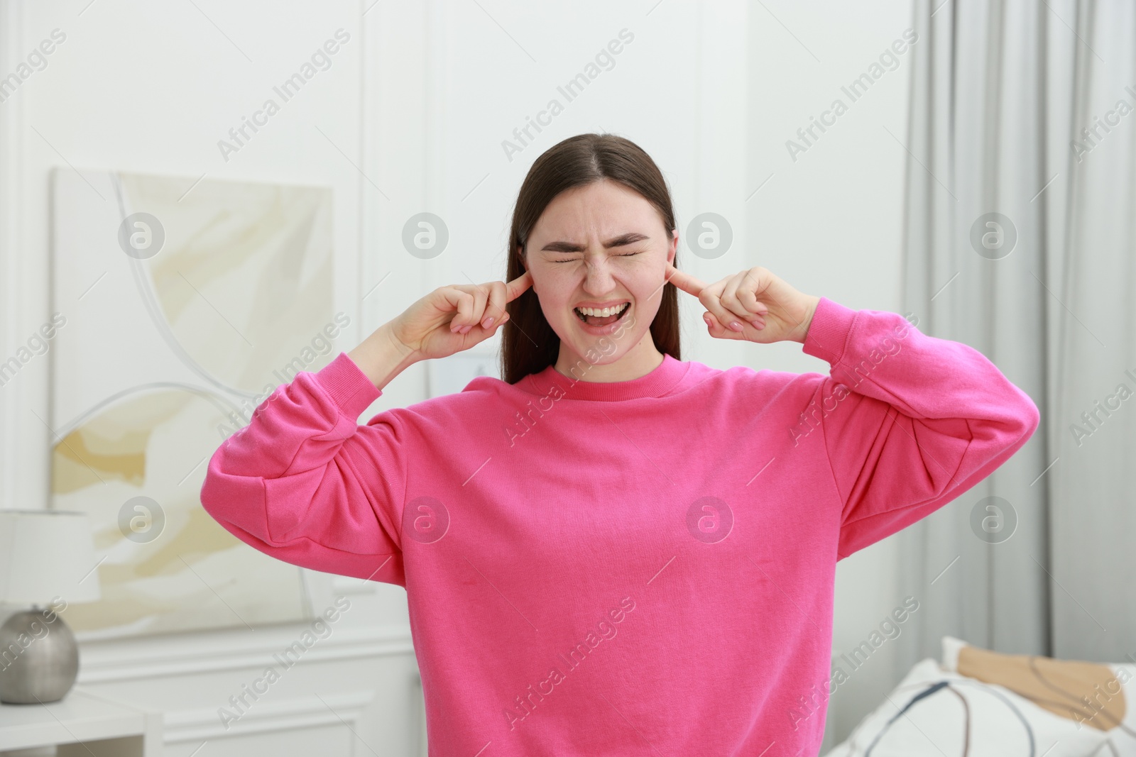 Photo of Frustrated woman covering her ears from loud noise at home