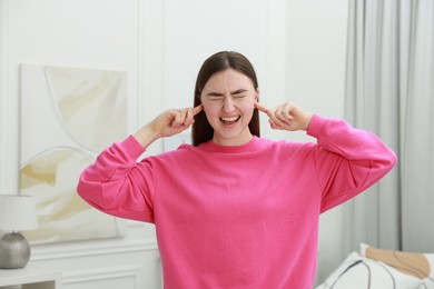 Frustrated woman covering her ears from loud noise at home